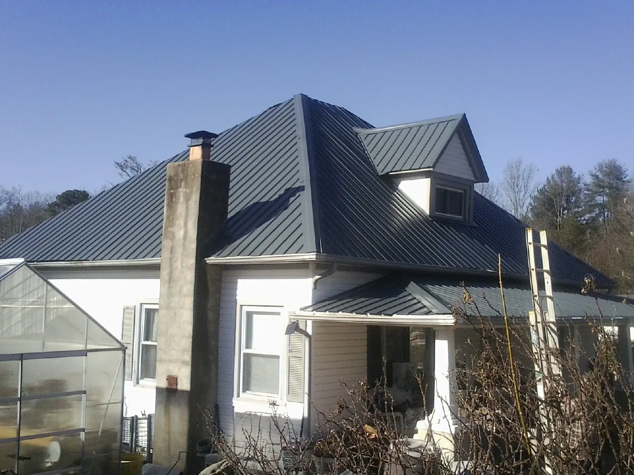 Dark blue standing seam metal roof on a white farmhouse with dormer — Slate & Tile Roof Repair by Roofing Brothers in Stevenson