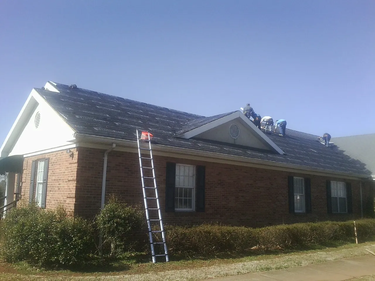 Crew tearing shingles off a brick ranch roof with a ladder set — Emergency Roof Repair work by our crew in Stevenson